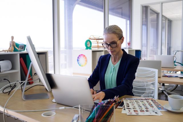 Female executive working at her desk in a modern office, using a computer. Ideal for depicting professional work environments, business productivity, corporate settings, and career-focused themes.