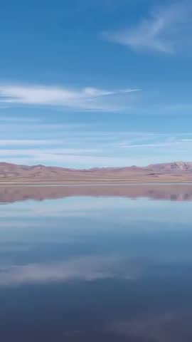 Panning vertical video revealing calm high-plain lake with mirrored sky and distant ridges