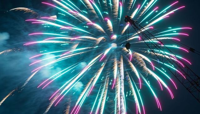 Teal and pink firework burst over construction crane silhouette at urban night celebration
