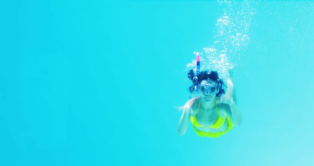 Brunette in yellow bikini swimming underwater wearing snorkel on her holidays