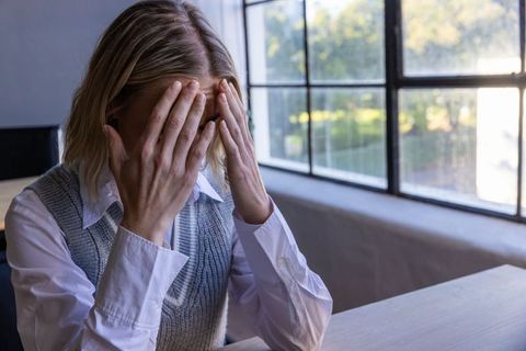 Stressed woman in office hiding face with hands at desk