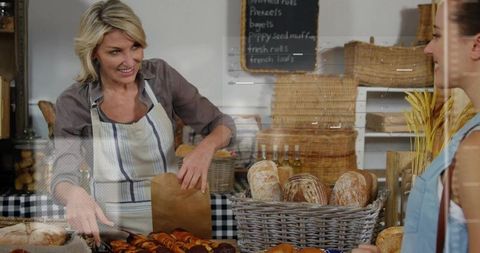 Smiling mature bakery vendor packing artisan bread and pastries at market counter with baskets