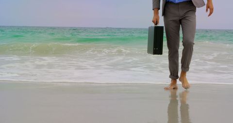 Businessman relaxing barefoot on beach with briefcase
