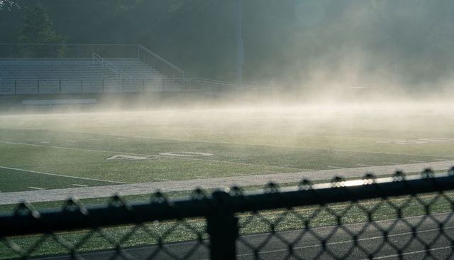 Foggy morning empty high school football field with bleachers and chain-link fence