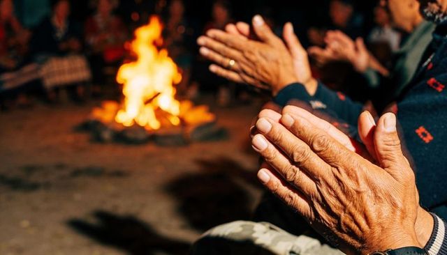 Senior hands warming by campfire at night, ring on finger, knitted sweater, warm glow