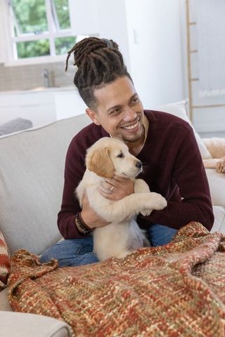 Man holding golden retriever puppy on couch smiling cozy living room moment