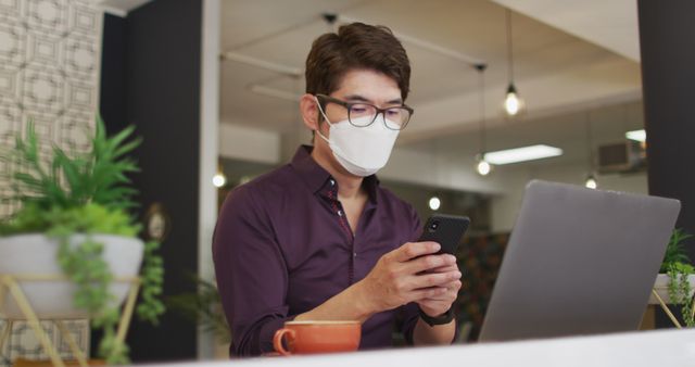 Young Asian professional wearing face mask using smartphone and laptop in modern office - Download Free Stock Images Pikwizard.com