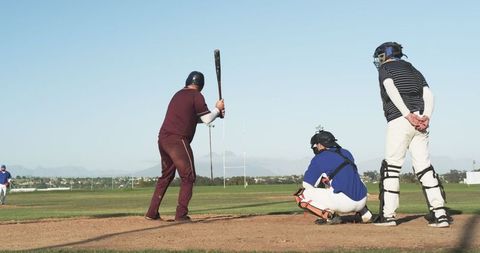 Male Batter Preparing to Swing Bat at Home Plate on Sunny Day