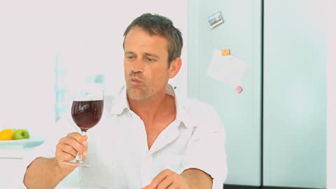 Man Savoring Red Wine in Kitchen Setting