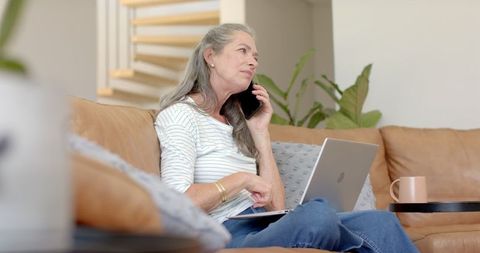 Senior Woman Chatting on Phone While Using Laptop