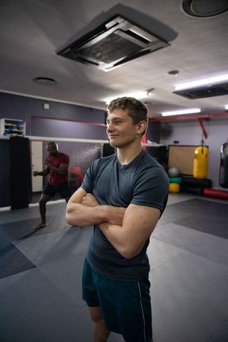 Confident mma fighter observing training partner in gym with punching bag and cage