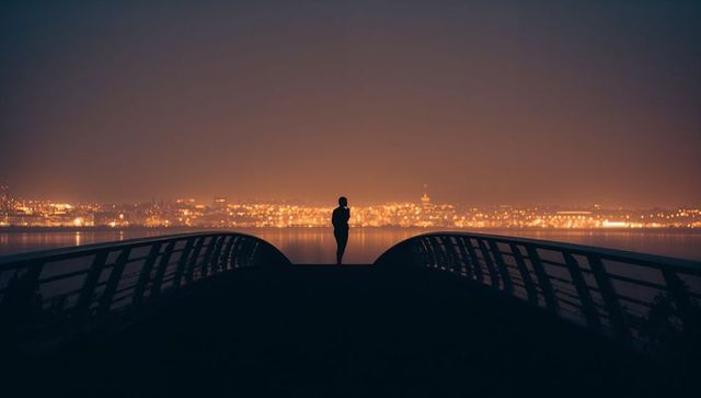 Silhouetted Figure on Bridge Overlooking City Lights at Night