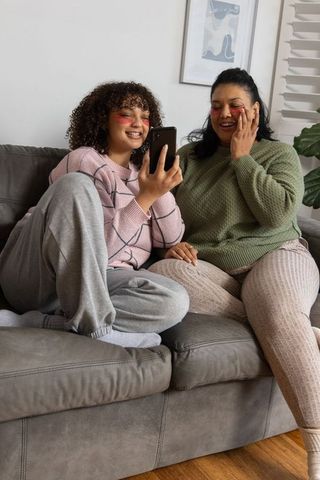 African american mother and daughter sharing skincare moment on couch, relaxing at home