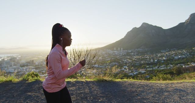 Woman jogging on an outdoor trail during sunrise with mountains in the background. The image highlights fitness and a healthy lifestyle, perfect for promoting outdoor exercise, fitness routines, morning workouts, and nature activities.