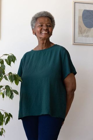 Senior african woman smiling and standing at home with plant and framed botanical print