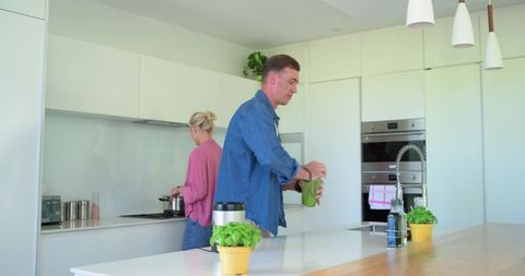 Couple cooking in modern minimalist kitchen, man blending smoothie, woman stirring