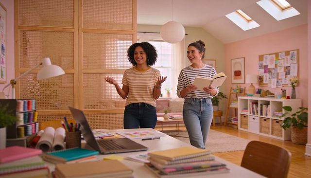 Two women collaborating in cozy home studio designing crafts, sketches and color swatches