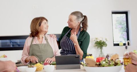 Senior women collaborating in kitchen with tablet and fresh vegetables