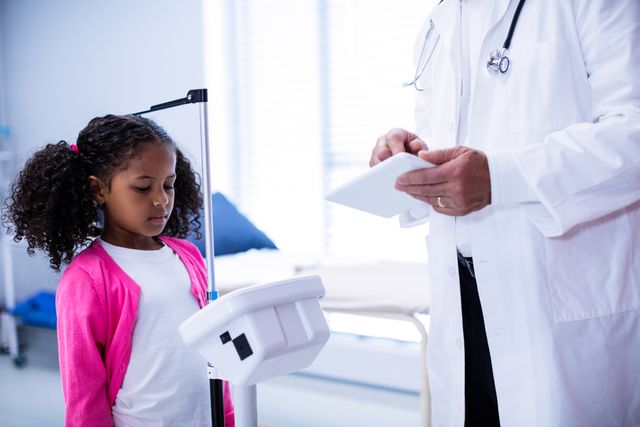 Image shows a doctor measuring the height of a young girl in a clinic using a digital tablet. Perfect for healthcare, medical checkups, pediatric care, and child health-related content.