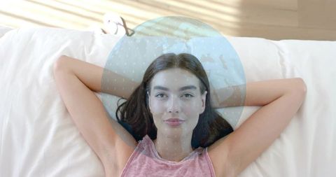 Relaxing young woman reclining on bed with globe overlay symbolizing global connection