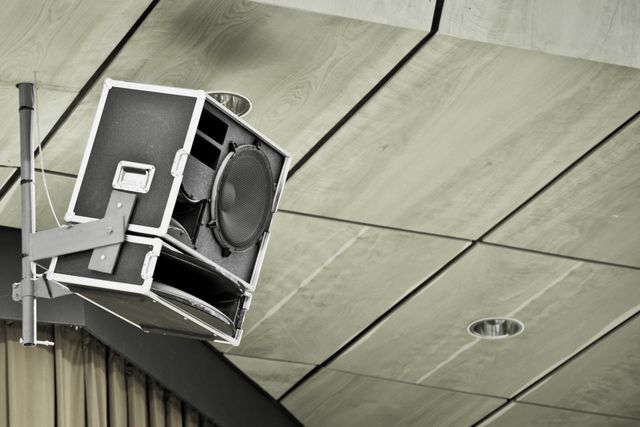Focused view of a ceiling mounted loudspeaker in a modern conference hall. Suitable for use in presentations about audio equipment, sound systems, professional audio setups, and conference room designs.