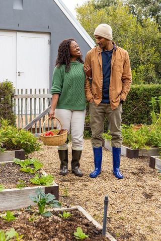 African american couple walking arm-in-arm through backyard vegetable garden with basket