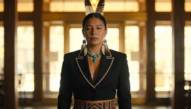 Standing indigenous woman wearing feather crown, turquoise necklace and bead-trimmed blazer