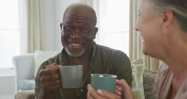 Happy senior diverse couple wearing shirts and drinking coffee in living room - Download Free Stock Photos Pikwizard.com