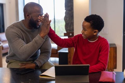 African american father and son high-fiving while learning with tablet at home