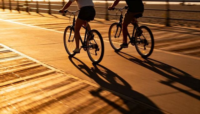 Golden hour cyclists riding boardwalk bikes casting long shadows on waterfront path