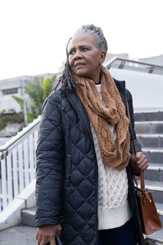 Senior african american woman pausing on stairs wearing coat and scarf holding handbag