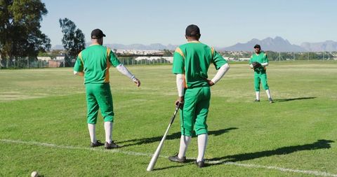 Practicing baseball teammates on sunlit grass field holding bat and glove