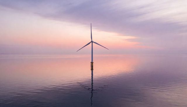 Solitary offshore wind turbine reflecting on calm pastel sea at twilight renewable energy