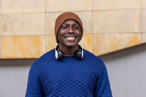 Smiling young man wearing brown beanie and headphones outside modern tiled facade