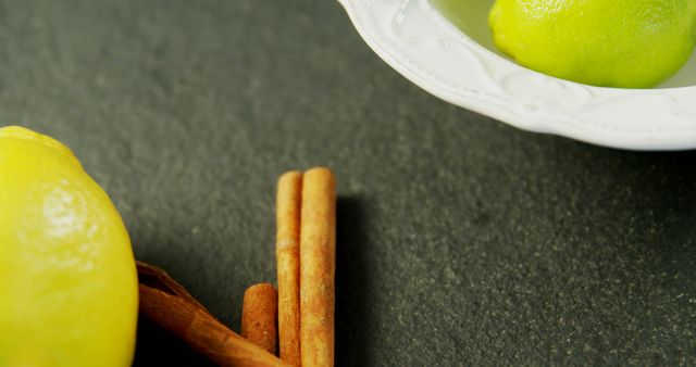 Lemons and cinnamon sticks are presented on a dark surface, with copy space. These ingredients are often used in cooking and baking to add a fresh and spicy flavor to dishes.