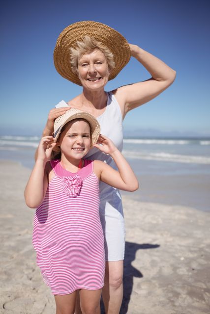 Portrait of girl with grandmother wearing sun hat at beach during sunny day