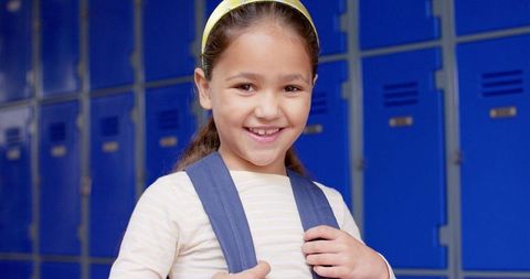Smiling Girl with Backpack in School Hallway by Blue Lockers