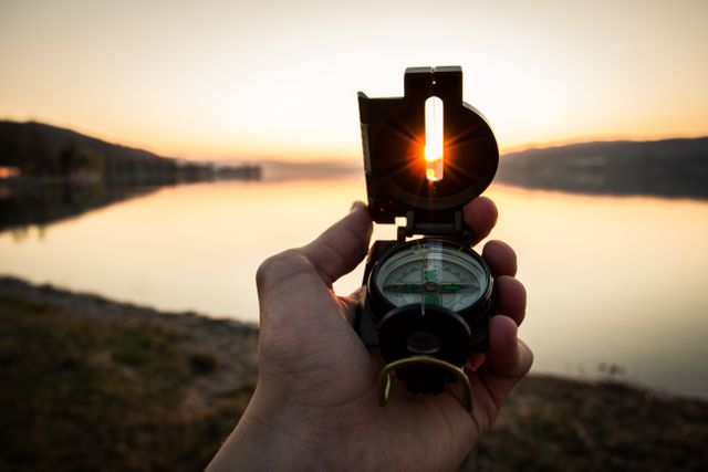Hand Holding Compass Overlooking Serene Lake at Sunset - Download Free Stock Photos Pikwizard.com