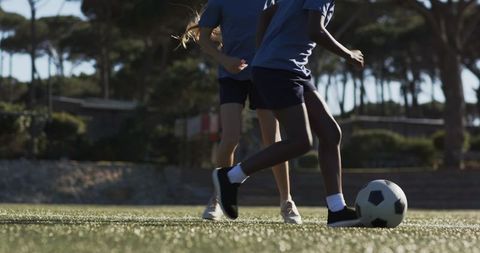 Diverse teenage soccer teammates controlling ball on turf in matching blue shirts