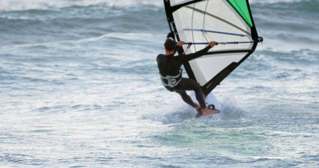 A man is windsurfing on rough ocean waves, showcasing action and adventure. This image is perfect for advertising water sports activities, promoting tourism, or illustrating articles related to beach vacations and outdoor adventures.