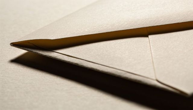 Minimal beige envelope showing triangular flap, seam, soft grain texture and dramatic shadow