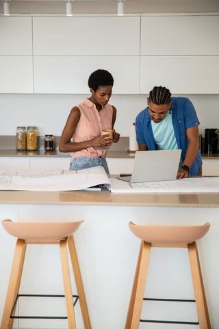 Couple Collaborating Over Blueprints in Kitchen Space