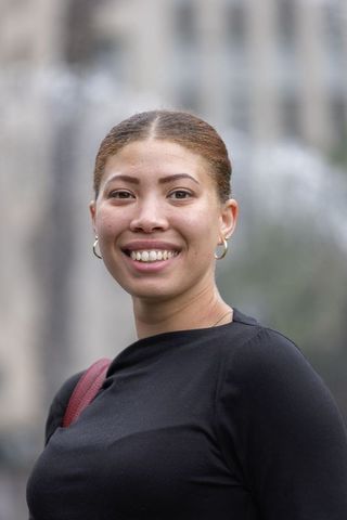 African american woman smiling in urban plaza wearing black fitted top, gold hoops
