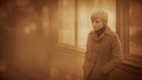 Contemplative teen in double-breasted coat by wooden window sepia vintage corridor mood