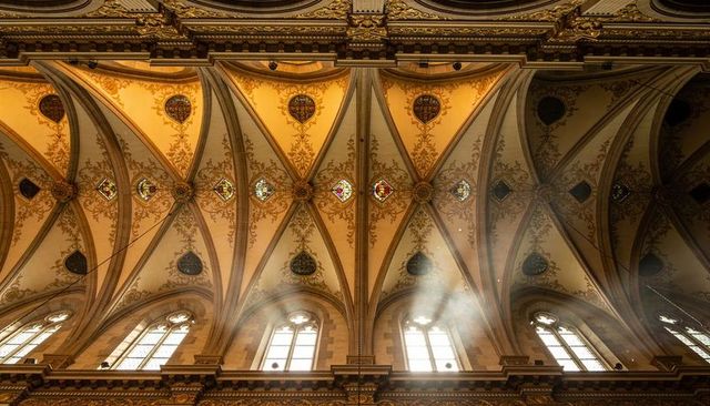 Sunlit gothic nave with ribbed vaults, stained-glass medallions, ornate gilded cornice