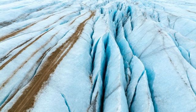 Aerial view of blue glacier crevasses with brown moraine streaks and ice ridges