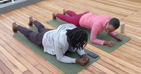 African American couple holding forearm plank on rooftop deck barefoot outdoor workout