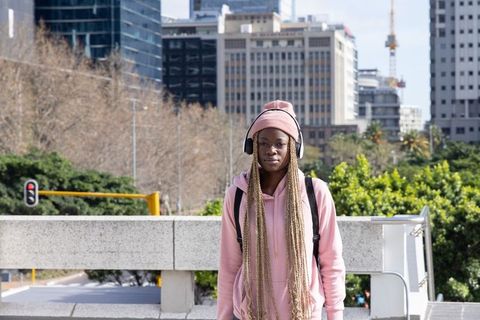 African American woman commuting in pink hoodie and beanie listening on urban overpass