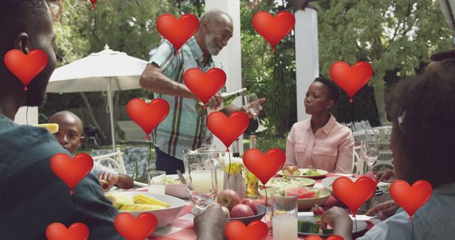 Image oh heart balloons over happy african american family dining in garden. family, love and communication technology concept digitally generated image.