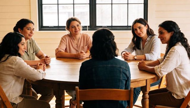 Leading woman guiding small group discussion around round wooden table in sunlit room